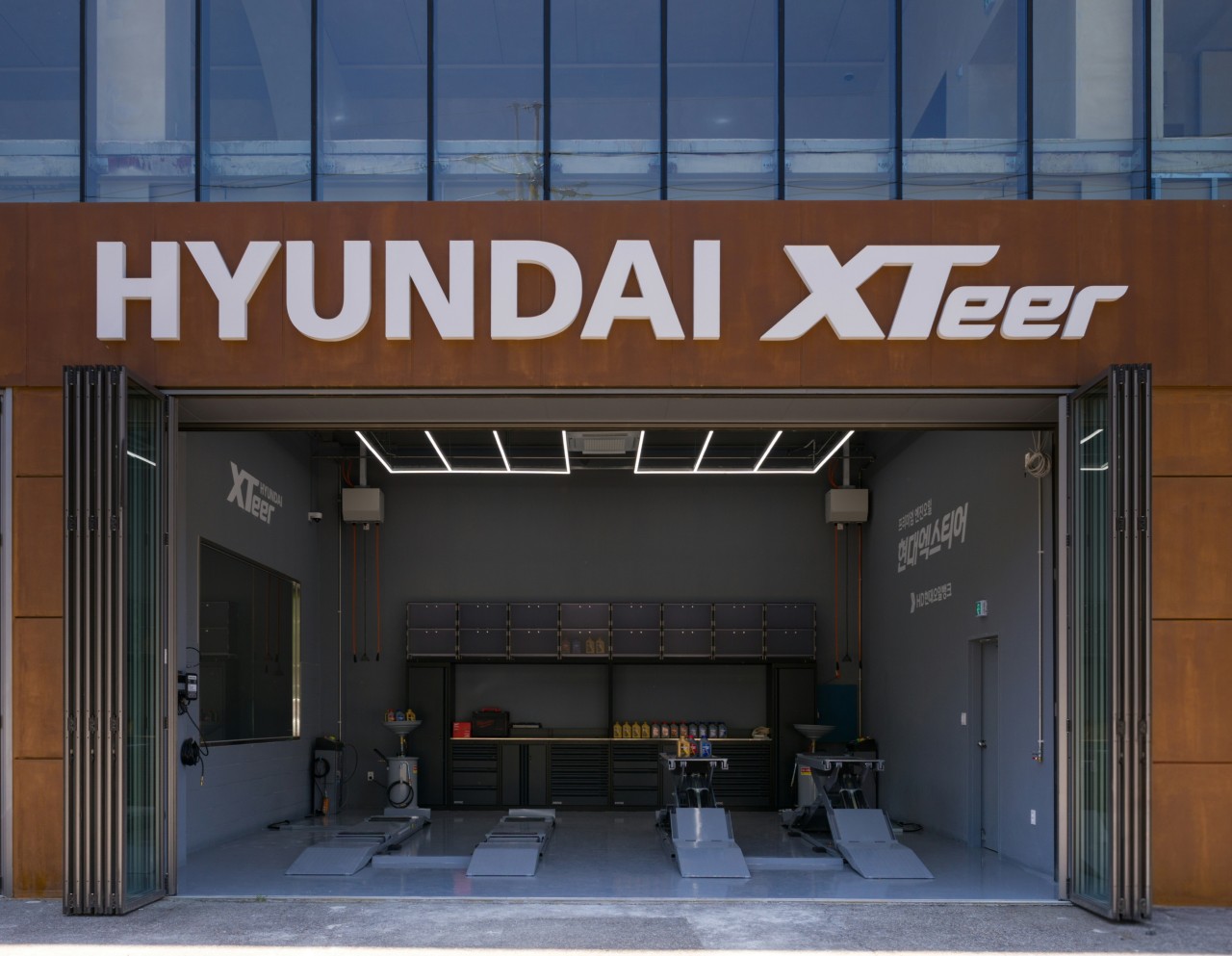 'HYUNDAI XTeer' 간판 아래 열린 정비 베이와 작업대에 놓인 엑스티어 오일